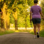 Man jogging and woman walking a dog on a picturesque outdoor path.