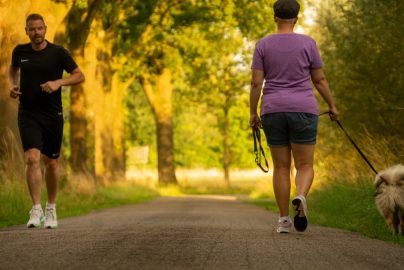 Man jogging and woman walking a dog on a picturesque outdoor path.